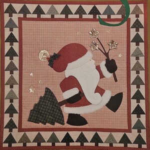 May include: A Christmas-themed craft pattern titled "Deck The Halls." The design features a Santa Claus applique with a Christmas tree and star accents. The border includes alternating Christmas trees. The background is a gold color.