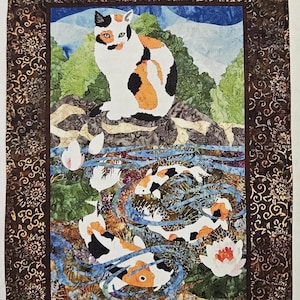 May include: A fabric quilt panel titled Something Fishy by Amy Loh Kupser featuring a calico cat looking at koi fish in a pond. The panel measures 14 inches by 22 inches, with a finished size of 17.5/8 inches by 25.5/8 inches including the border.