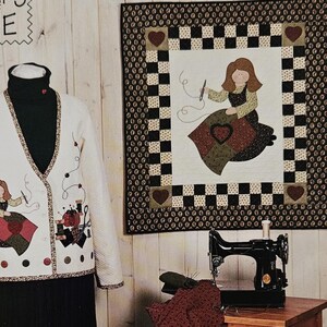May include: A cream-colored quilted jacket with an applique of a person sewing, a black skirt, a matching cream quilted tote bag with sewing motifs, a wall hanging with a similar applique, and a black sewing machine on a wooden table.