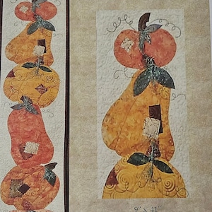 May include: A quilt pattern for a stack of pumpkins in various shades of orange, yellow, and red. The pattern is called "Pumpkin Stack" and is 9 inches by 41 inches. It is a design by Karon Trybom for Kreative Threads.