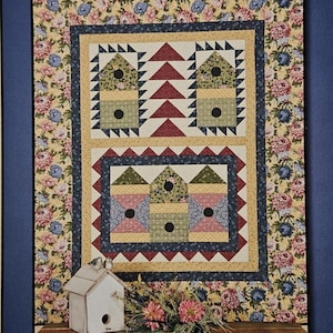 May include: A quilt pattern with the text "Garden Village" and "Thimbleberries". The quilt design features birdhouses and triangles, with dimensions of 56 x 70 inches. The background has a floral pattern.