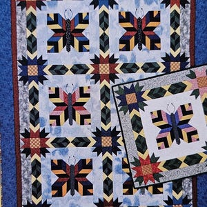 May include: A colorful quilt with a butterfly pattern. The quilt features a blue border, with a repeating pattern of butterflies and star-like shapes in shades of red, yellow, black, and blue. A smaller matching quilt is also present.