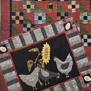 May include: A quilted wall hanging pattern titled "All Through the Night." The design features a red and green patchwork quilt with a smaller quilt depicting chickens, sunflowers, and eggs. The dimensions of the smaller quilt are 27" x 33".