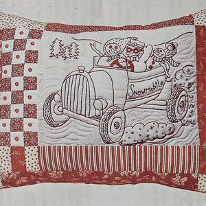 May include: Rectangular pillow with a quilted design. The center features a red and white illustration of a car labeled "Snowmobile" with three snowman passengers. The border has a patchwork and striped pattern in red and white.