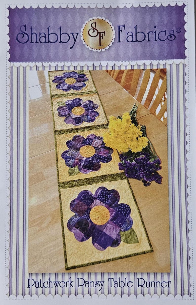 Op de afbeelding: Een patchwork tafelloper met grote paarse viooltjesbloemmotieven en gele centra op een lichtgele achtergrond. De loper is omrand met groen en heeft de tekst "Patchwork Pansy Table Runner". De bovenkant van de afbeelding heeft de tekst "Shabby Fabrics".