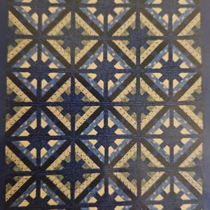 May include: A quilt with a geometric pattern in shades of blue, black, and white. The quilt is made up of squares and diamonds, and the pattern is repeated throughout the quilt.