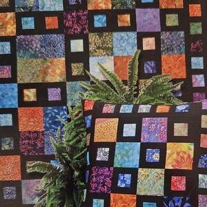May include: A colorful patchwork quilt with a black grid pattern. The quilt is made of squares of different fabrics, including floral prints, geometric patterns, and solid colors. A pillow with a similar design is in the foreground.