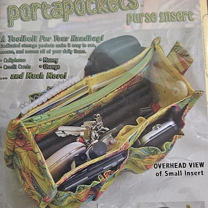 Pu&ograve; includere: Un inserto per borsa colorato, chiamato "portapockets", con pi&ugrave; tasche e cerniere. L'inserto contiene oggetti come un cellulare, chiavi e un taccuino. Il testo sull'inserto recita "A Toolbelt For Your Handbag!" e "purse insert."