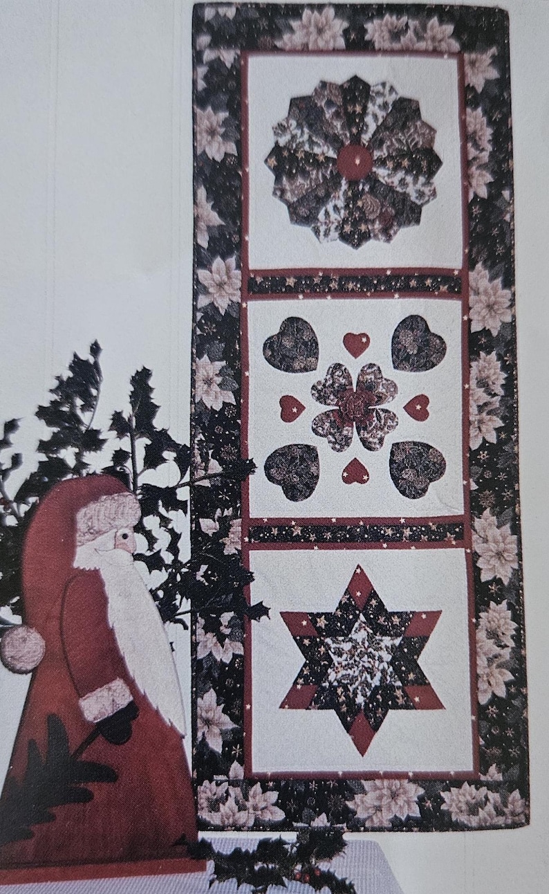 May include: A white quilted table runner with three different designs: a star, a flower, and a heart. The designs are made of black, red, and gold fabric. The runner is framed with a black and white floral border.