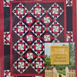 May include: A quilt with a red, black, and white geometric pattern. The quilt is framed by a black and red border. A book titled "Apart at the Seams" by Marie Bostwick is visible in the lower right corner of the image.