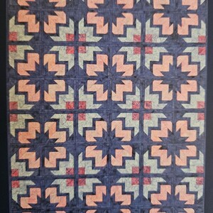 May include: A quilt with a repeating pattern of arrows in shades of pink, green, and blue. The arrows are arranged in a starburst pattern.