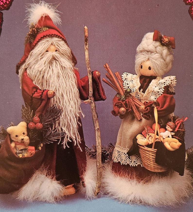 May include: A pair of handmade Christmas ornaments depicting Santa Claus and Mrs. Claus. Santa is holding a wooden staff and a bag of toys. Mrs. Claus is holding a basket of toys and a bundle of cinnamon sticks.