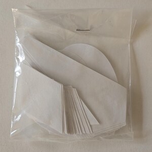 May include: A package of white adhesive fabric patches in various shapes, including squares, triangles, and circles. The patches are packaged in a clear plastic bag.