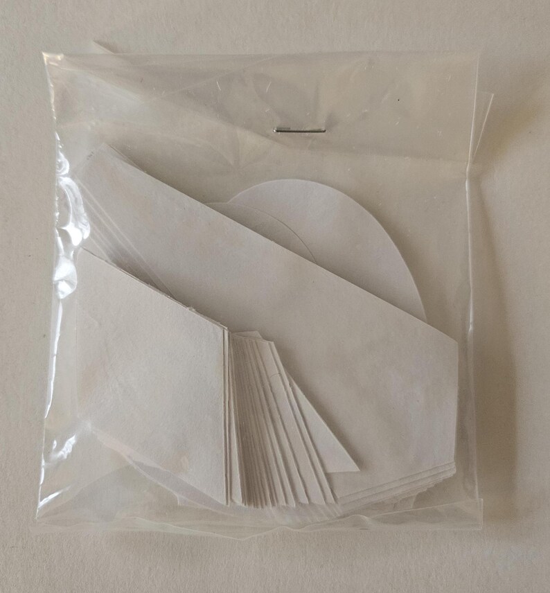 May include: A package of white adhesive fabric patches in various shapes, including squares, triangles, and circles. The patches are packaged in a clear plastic bag.