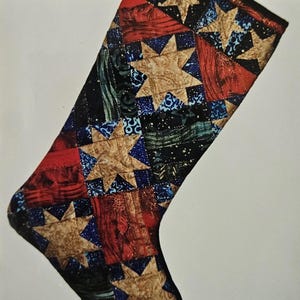 May include: A quilted Christmas stocking with a patchwork design. The stocking features a variety of fabrics in red, blue, black, and gold, with star patterns. It has a loop for hanging.