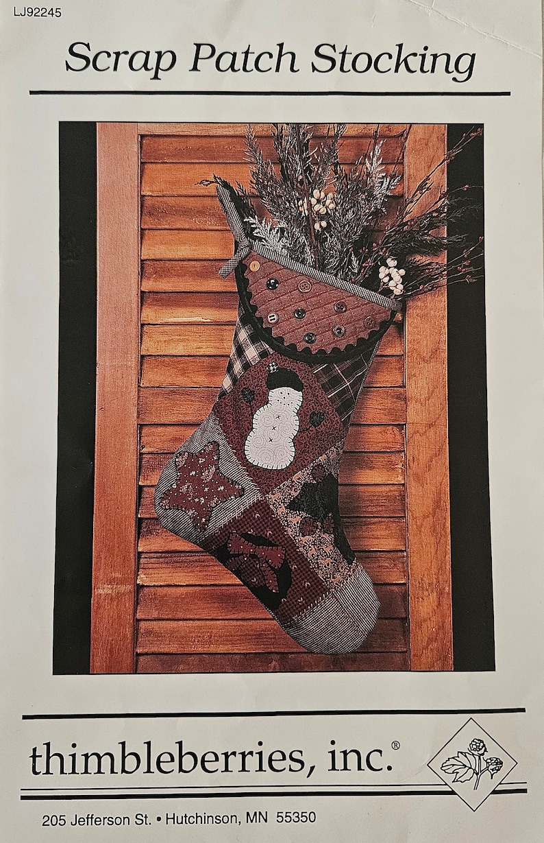 May include: A patchwork Christmas stocking with a snowman design, hanging on a wooden door. The stocking is made of various fabrics in shades of brown, red, and black. The stocking is decorated with buttons and a black ribbon.