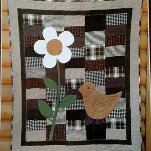 May include: A brown and white patchwork quilt with a white flower and a brown bird applique. The quilt is framed with a brown and white border.