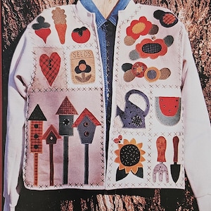May include: A white jacket with a variety of colorful appliques sewn on the front. The appliques include a heart, a flower, a watering can, a watermelon, a sunflower, a birdhouse, and gardening tools. The text "SEEDS" is also included on the jacket.