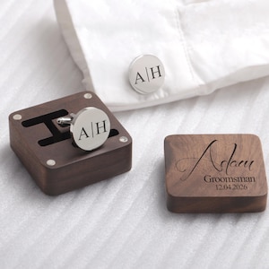 May include: A wooden box with a pair of silver cufflinks engraved with the initials "A|H". The box is made of dark wood and has a hinged lid. The cufflinks are in a small compartment inside the box. A second wooden box with the name "Adam" engraved on it, along with the word "Groomsman" and the date "12.04.2026".