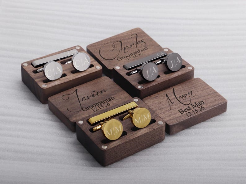 May include: Five wooden boxes with engraved names and dates. Each box contains a tie clip and cufflinks. The boxes are made of dark wood and have a polished finish.
