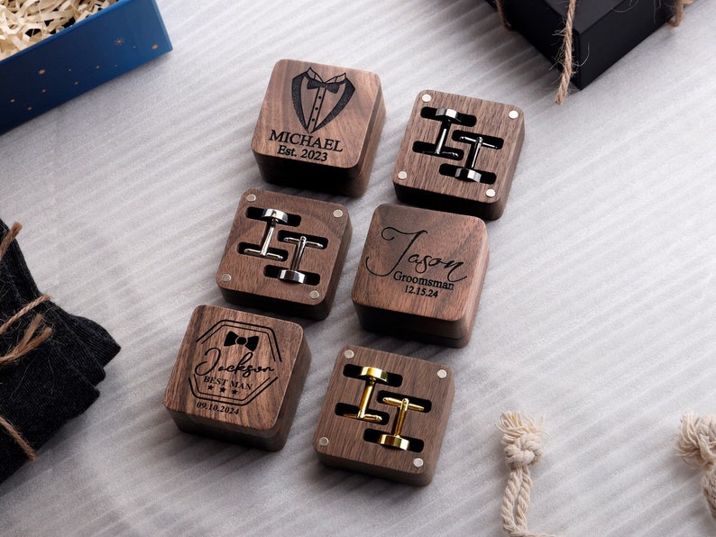 May include: Six wooden boxes with engraved text and cufflinks. The boxes are dark brown and have a polished finish. The text on the boxes includes names, dates, and titles such as "Best Man", "Groomsman", and "Michael Est. 2023".