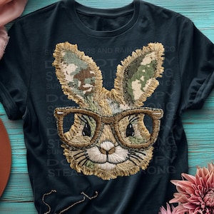 May include: A navy blue t-shirt with an embroidered bunny wearing glasses. The bunny's ears have a camouflage pattern. The text on the shirt reads "SUN, DO, STEA, STRONG".
