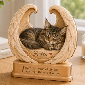May include: A light brown wooden memorial sculpture featuring a sleeping tabby cat nestled within a pair of carved angel wings. The base is engraved with the text, I loved you your whole life, I'll miss you the rest of mine, and Bella with a red heart.