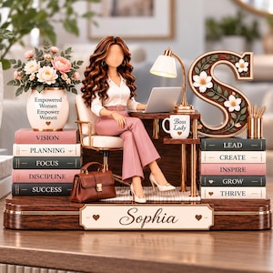 May include: A decorative desk figurine featuring a brown-haired figure sitting at a desk with a laptop, a lamp, and a mug labeled Boss Lady. The base is personalized with the name Sophia and stacks of books labeled Vision, Planning, Focus, Discipline, Success, Lead, Create, Inspire, Grow, and Thrive.