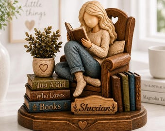 Könnte beinhalten: Eine Figur einer Person mit langem blondem Haar, die in einem Holzstuhl sitzt und ein Buch liest. Die Person trägt einen beigen Pullover und eine blaue Jeans. Ein Stapel Bücher trägt die Aufschrift Just A Girl Who Loves Books.