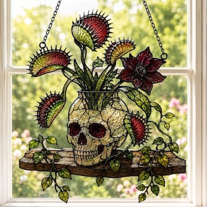 May include: A stained glass suncatcher featuring a human skull planter resting on a wooden shelf. The skull holds several red and green Venus flytrap plants and a dark red flower. The piece is suspended by two black metal chains for window display.