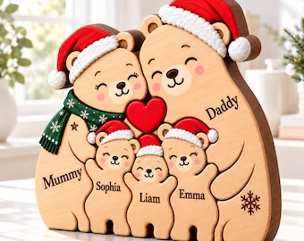 Könnte beinhalten: Ein Bärenfamilien-Puzzle aus Holz mit zwei großen und drei kleinen Bären, die rote Weihnachtsmützen mit weißem Rand tragen. Die Bären sind mit den Namen Mummy, Daddy, Sophia, Liam und Emma graviert. Ein grüner Schal und ein rotes Herz sind dabei.