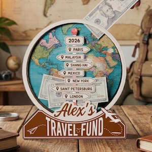 Op de afbeelding: Een houten reisgeld display met een wereldkaart ontwerp. De display heeft een gleuf voor het insteken van geld, een bord met de tekst "Alex's Travel Fund" en bestemmingsmarkeringen voor steden als Parijs. Een hand steekt een twintig dollar biljet in de gleuf.