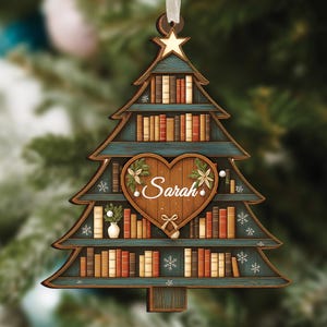 Op de afbeelding: Houten kerstboomornament met een boekenplankontwerp. Het ornament heeft een hartvormig midden met de naam "Sarah" en bloemaccenten. De boom is geschilderd in blauw en bruin, met een ster aan de bovenkant.