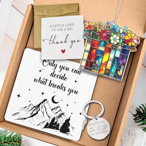 May include: A gift box containing a card that says "Thank you", a mountain-themed square plaque with the text "Only you can decide what breaks you", a keychain with the text "If I can't take my book I'm not going", and a stained glass-style pendant.