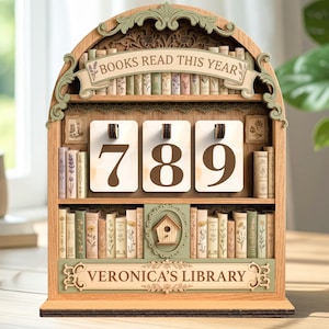 May include: Wooden bookshelf-shaped counter with the text "BOOKS READ THIS YEAR" and the numbers "789". The bookshelf has decorative elements and the text "VERONICA'S LIBRARY". The design includes miniature book illustrations and a birdhouse.