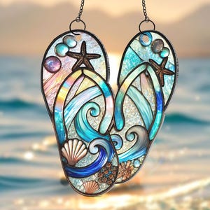 May include: A stained glass suncatcher shaped like a pair of flip flops with a beach scene. The flip flops are blue, green, and white with seashells, starfish, and waves.