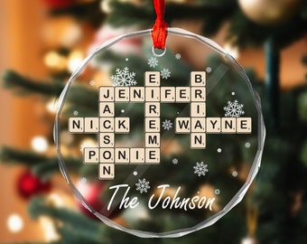 May include: A clear glass Christmas ornament with a scrabble tile design spelling out the names "Jennifer", "Nick", "Wayne", "Ari", and "Ponie". The ornament also includes the text "The Johnson" and snowflakes.
