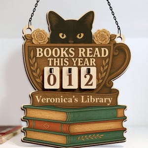 May include: Wooden sign with a black cat peeking over a teacup design. The sign reads "BOOKS READ THIS YEAR" with a counter showing "012". Below the counter is "Veronica's Library". The sign is hanging by a chain.
