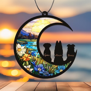 May include: A stained glass moon ornament with a sunset scene and three dog silhouettes. The dogs are labeled "Guave", "Alain", and "Henry".