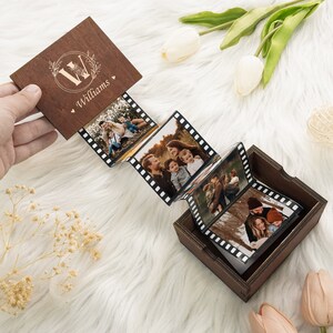 May include: A wooden box with a personalized engraved lid featuring the letter "W" and the name "Williams". The box contains a photo album with black and white film strips, each holding a photo of a family.