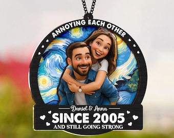 May include: A circular wooden ornament featuring a couple embracing, set against a starry night backdrop. The text "ANNOYING EACH OTHER" is at the top. Below, it reads "Daniel & Anna SINCE 2005 AND STILL GOING STRONG."
