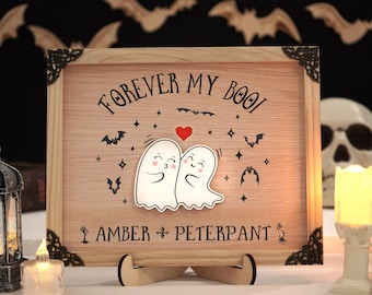 Może przedstawiać: Drewniany znak z napisem "Forever My Boo!" i dwoma kreskówkowymi duchami, które się całują. Znak jest ozdobiony nietoperzami i gwiazdami. Pod duchami widnieją imiona "Amber + Peterpant".