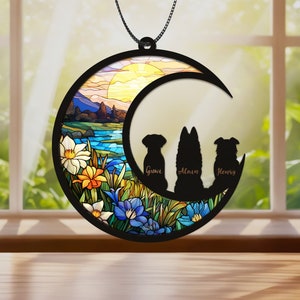 May include: A stained glass style moon ornament with a sunset scene and three dog silhouettes. The dogs are named "Guavi", "Alain", and "Henry".