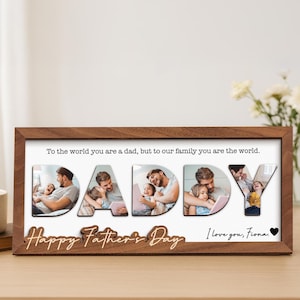 Op de afbeelding: Een houten fotolijst met het woord "DADDY" gespeld in afzonderlijke letters, elk met een andere foto van een vader en kind. De lijst heeft de tekst "To the world you are a dad, but to our family you are the world." en "Happy Father's Day I love you, Fiona."