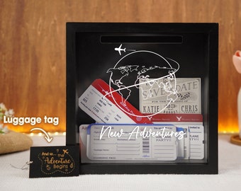 May include: Black shadow box with a white globe and airplane design. The box contains several airline boarding passes and a save the date card that reads "KATIE & CHRIS". A luggage tag with the text "And so... the Adventure Begins" is in the lower left corner of the image.