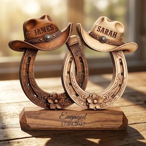 May include: A wooden decorative piece featuring two interlocking horseshoes, each topped with a cowboy hat. The left hat is engraved with the name JAMES and the right with SARAH. The base is engraved with the text Engaged 17.04.2027.