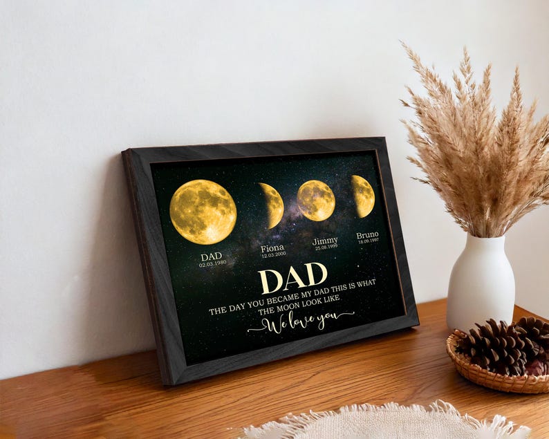 May include: Framed art print featuring a celestial design with moon phases and the word "DAD" in large text. The print includes dates and names, with the phrase "We love you" at the bottom. The frame is black.