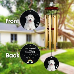 May include: A black and white wind chime with a round, black disc featuring a white dog and the text "Hear the wind and think of me in your heart I'll always be Alain". The disc is attached to a gold metal wind chime with a wooden top.