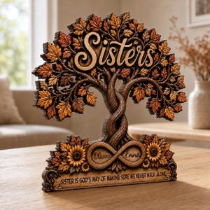 May include: A wooden decorative tabletop sign shaped like a tree with autumn-colored leaves. The word Sisters is carved at the top. An infinity symbol at the base contains the names Olivia and Emma. The text reads, Sister is God's way of making sure we never walk alone.