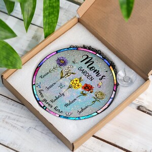 May include: A round glass suncatcher with a blue, green, and purple stained glass design. The suncatcher features a floral design with butterflies and the text "Mom's Garden". The names Kevin, Jessica, Kimberly, Melissa, and Joshua are written around the edge of the suncatcher.